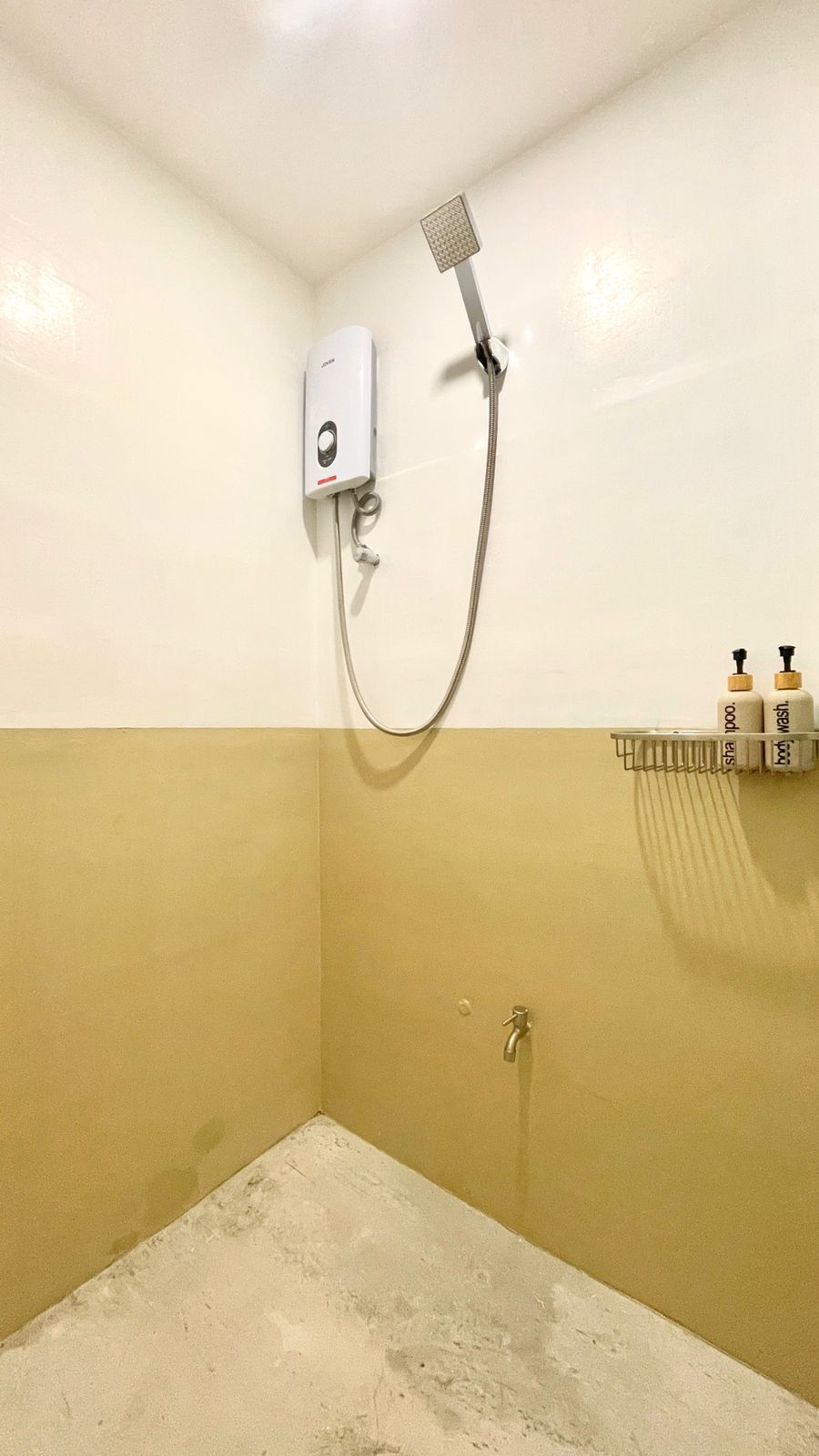 Shower stall with two-tone yellow walls. A showerhead, water heater, and toiletries are visible.