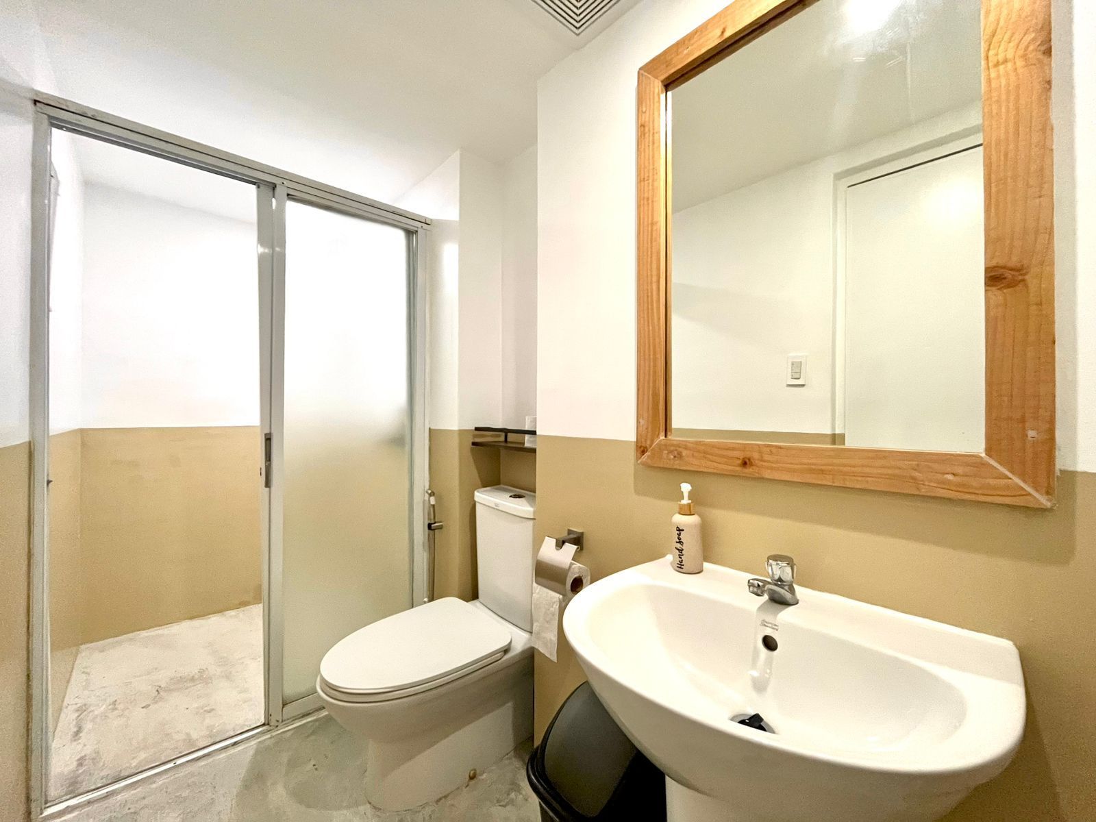 Bathroom with a white sink, toilet, and shower stall. Wooden-framed mirror and tan/white walls.