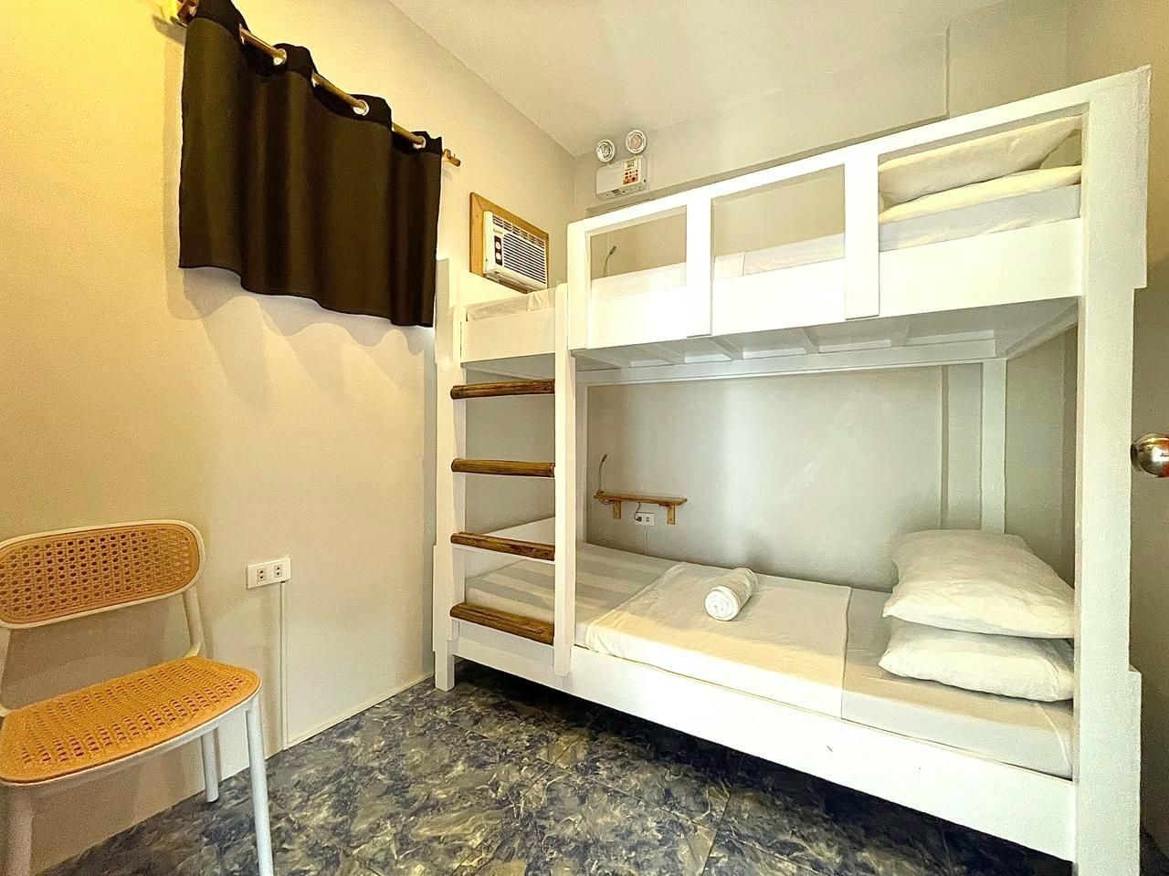 Bunk bed in a small, plain room with a chair, window curtain, and air conditioning unit.