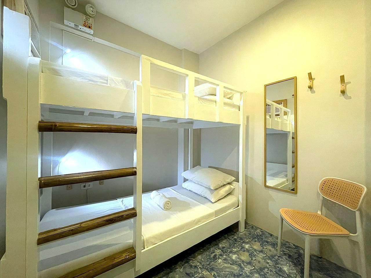 White bunk beds in a room, with a mirror, chair, and hooks on the wall.