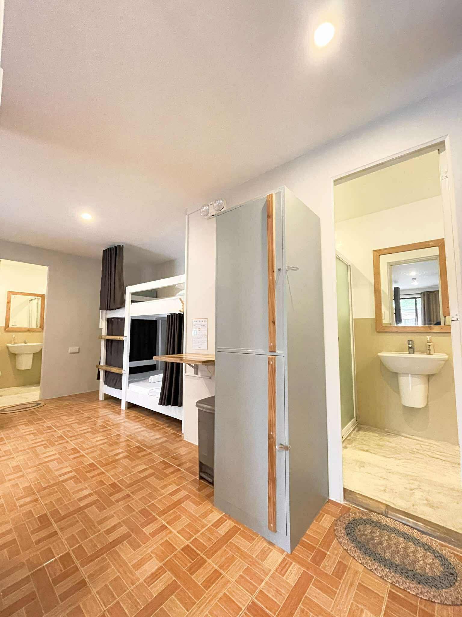 Hostel dorm room: bunk beds, refrigerator, two sinks, and an open doorway.