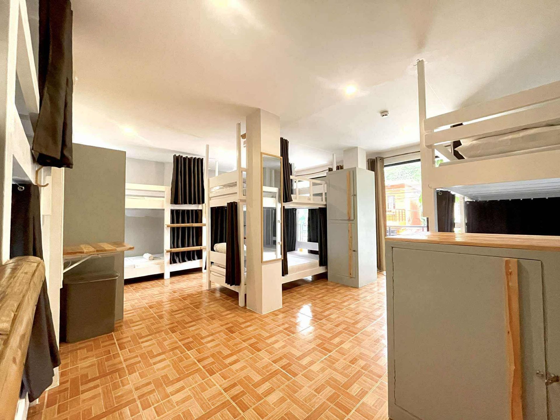 Dorm room with multiple bunk beds, gray storage units, and wooden floors.