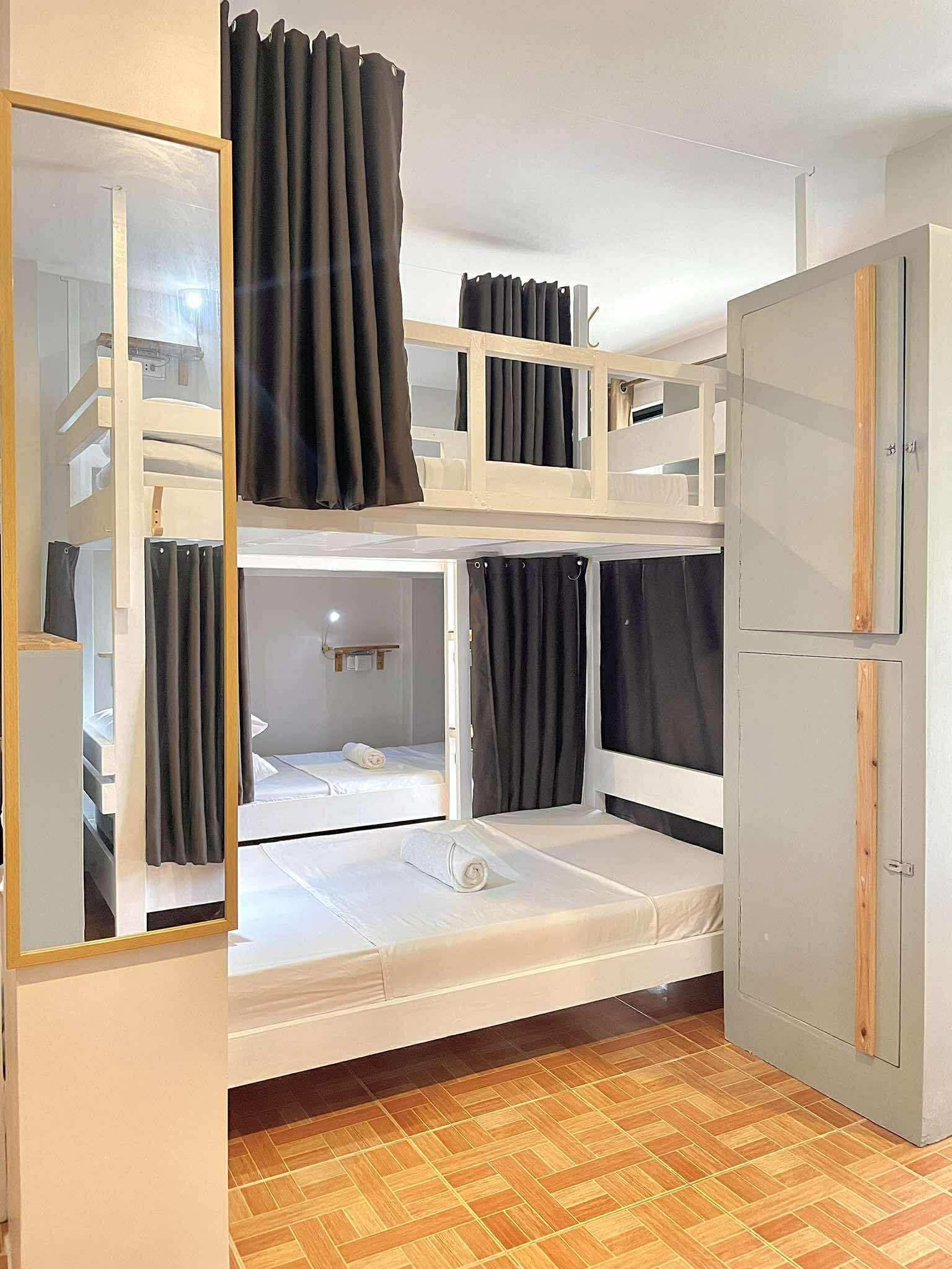 Bunk beds with curtains in a light-filled room; hardwood floors, gray wardrobe, and a large mirror are visible.