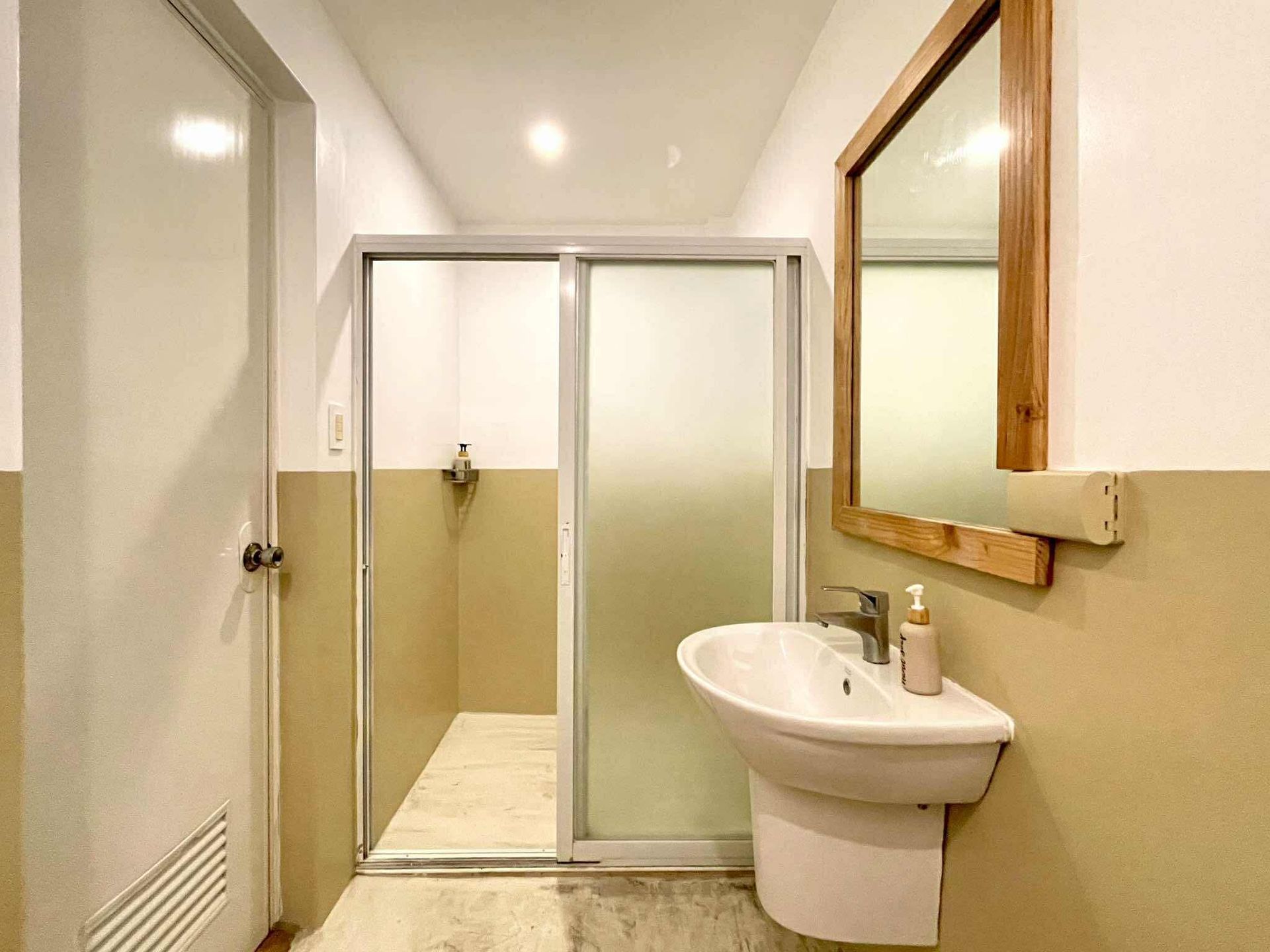 Bathroom with white walls, a sink, mirror, shower, and closed door.
