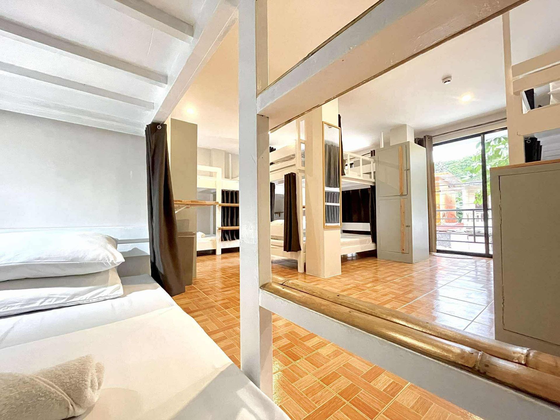 Hostel room with multiple bunk beds, neutral-toned walls, and a balcony view.