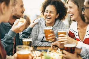 Friends laughing and drinking beer at an outdoor table.