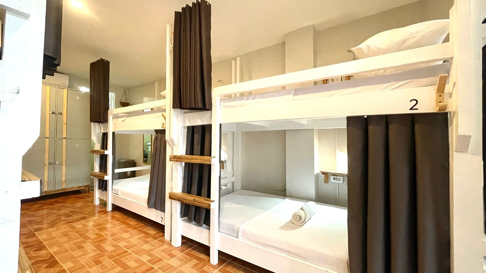 Bunk beds in a hostel room. Each bed has a privacy curtain, ladder, and a number.