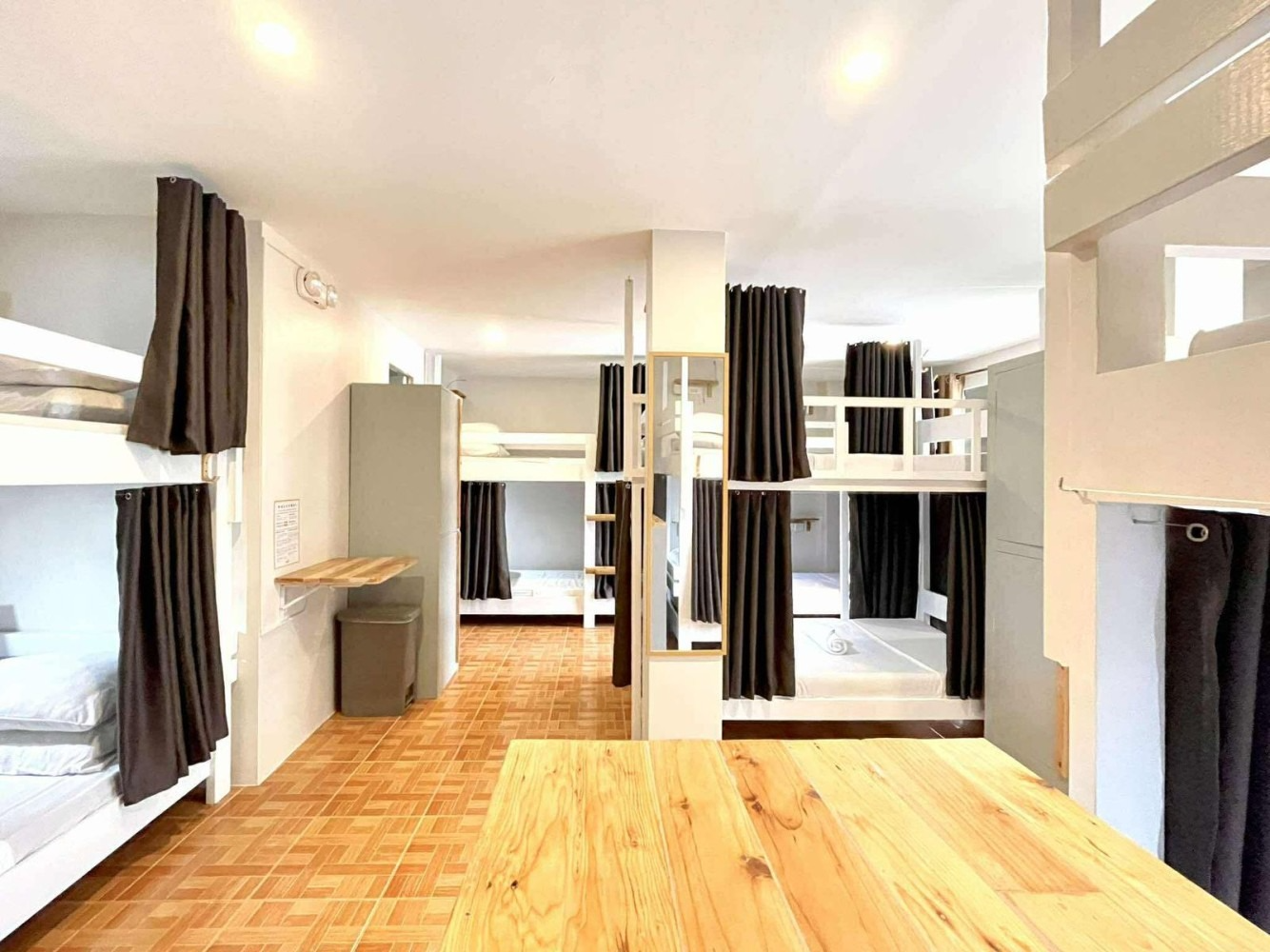 Hostel dorm room with multiple bunk beds, gray curtains, and wooden floor.