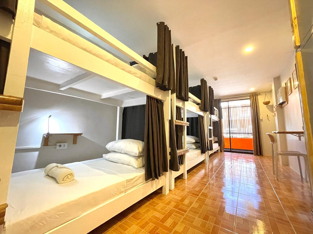 Hostel dorm room with multiple bunk beds, brown curtains, and tiled floor.