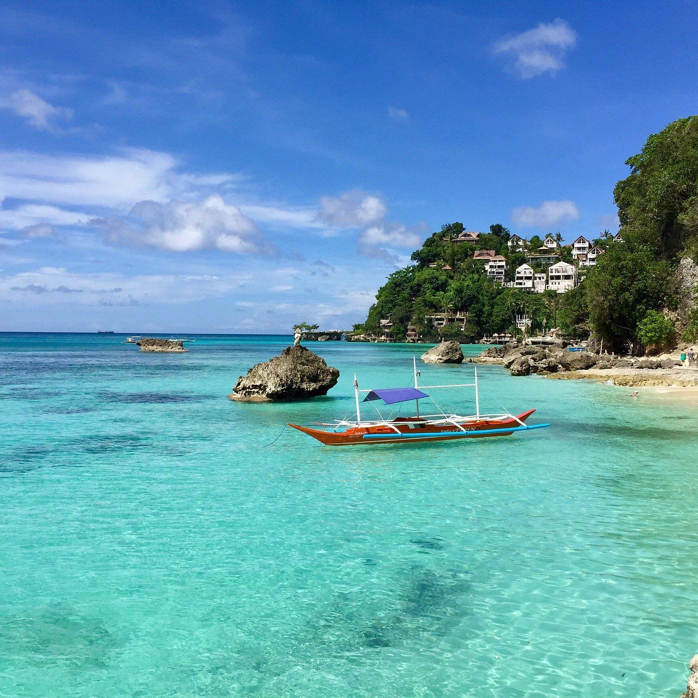 Turquoise water, a boat, and a rocky coastline under a blue sky.