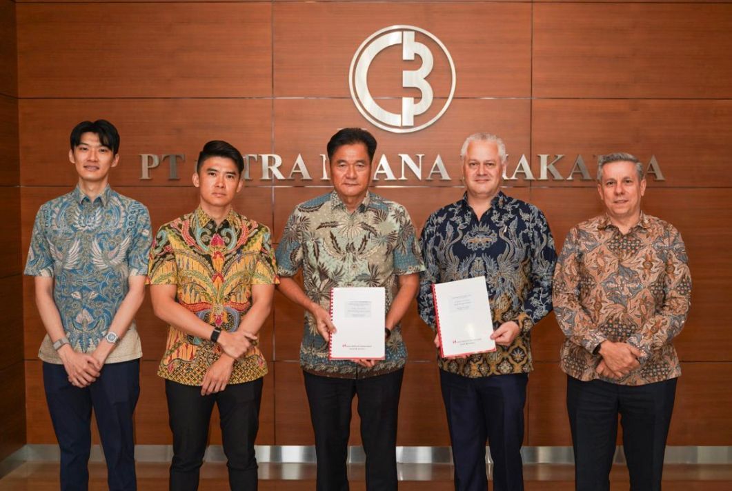 Six men in patterned shirts and dark pants holding documents, standing in front of a company logo.