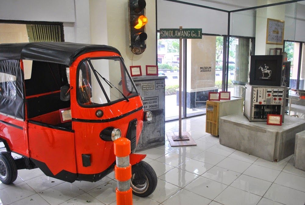 A red rickshaw is parked in a room next to a traffic light.