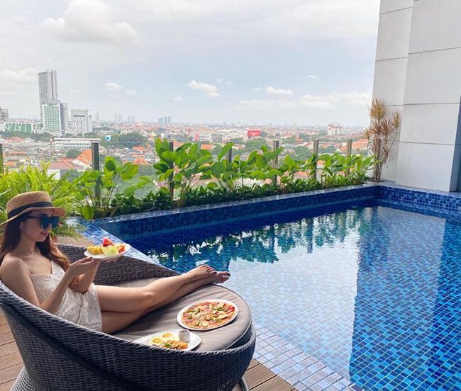 A woman is sitting in a chair next to a swimming pool holding a plate of food.
