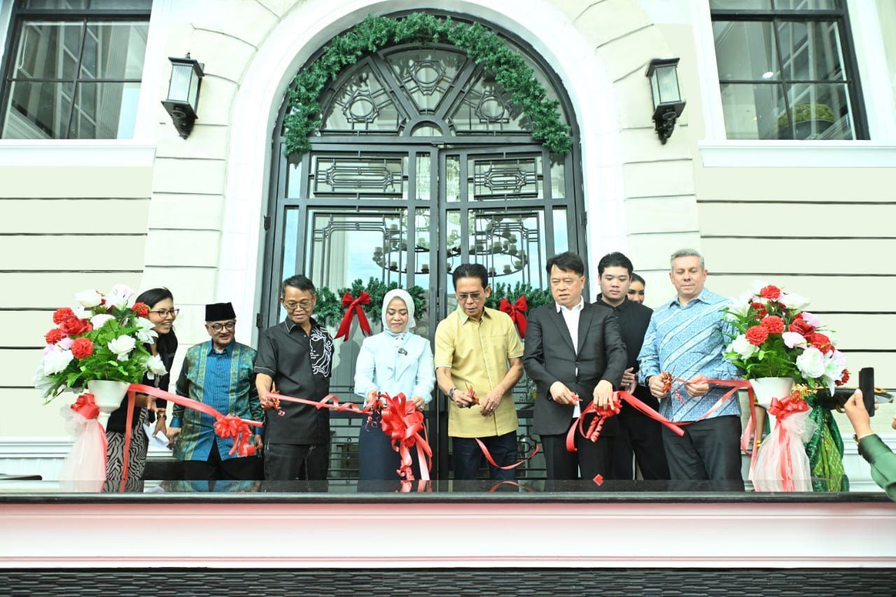 Four people at signing ceremony, two shaking hands. Backdrop reads 