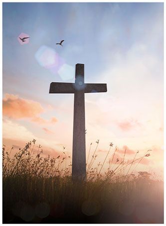 A cross is standing in the middle of a field at sunset.