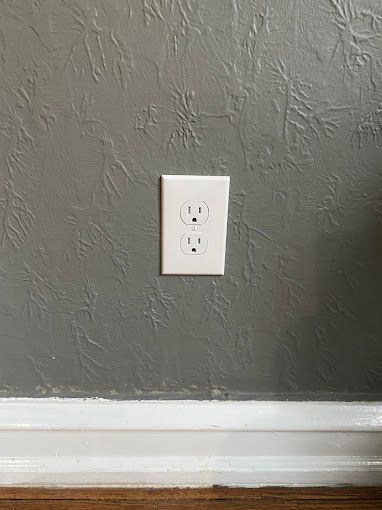 A white electrical outlet is sitting on a gray wall.