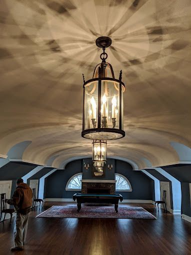 A man is standing in a room with a chandelier hanging from the ceiling.