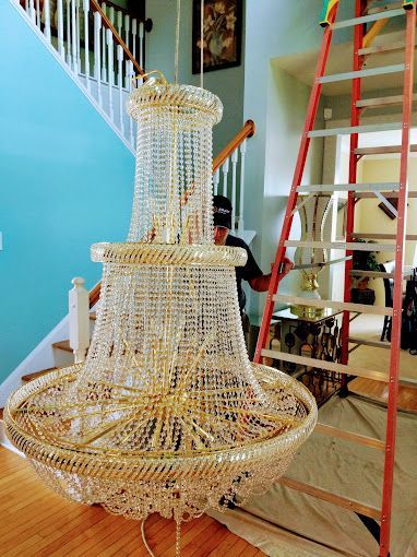 A man is standing on a ladder next to a large chandelier in a living room.