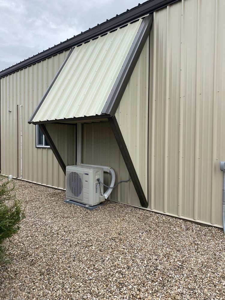 Metal building with tan siding, awning over an air conditioning unit.