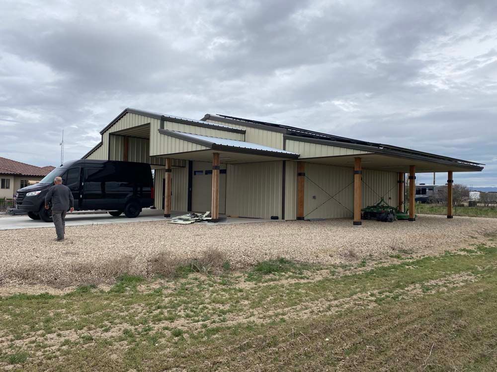 A person walks towards a black van parked near a tan barn-style building with a covered awning, cloudy sky.