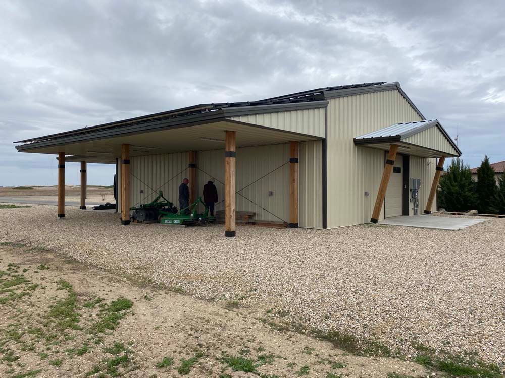Beige metal building with a covered awning, two figures, gravel ground.