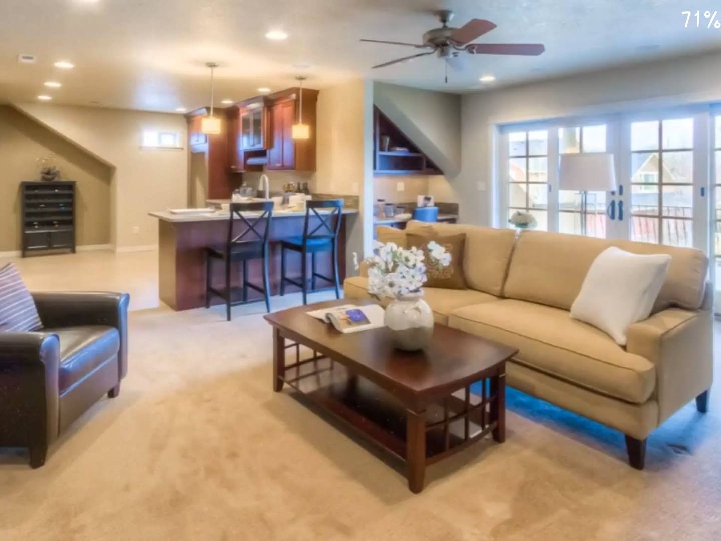 Cozy living room with open kitchen, tan walls, couch, coffee table, and French doors to a deck.