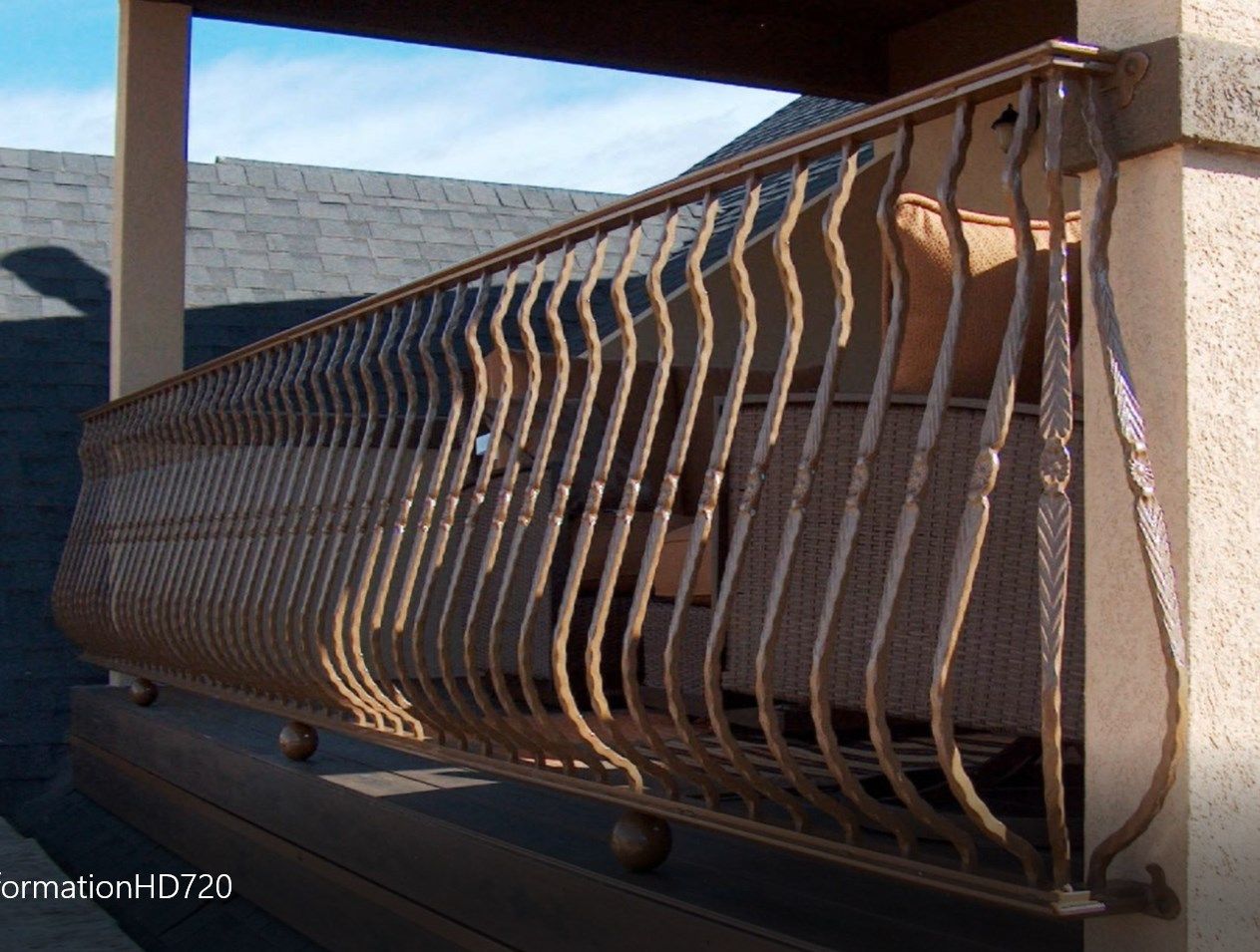 Bronze metal balcony railing on a porch. The railing has a wave-like pattern.