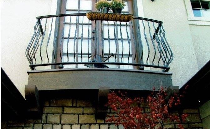 Balcony with wrought iron railing, flower box, and French doors on a beige building.