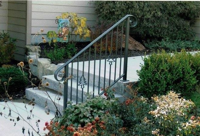 Exterior concrete steps with decorative wrought iron handrail. Landscaping surrounds.