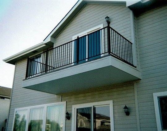 Exterior view of a house with a small black-railed balcony above sliding glass doors.