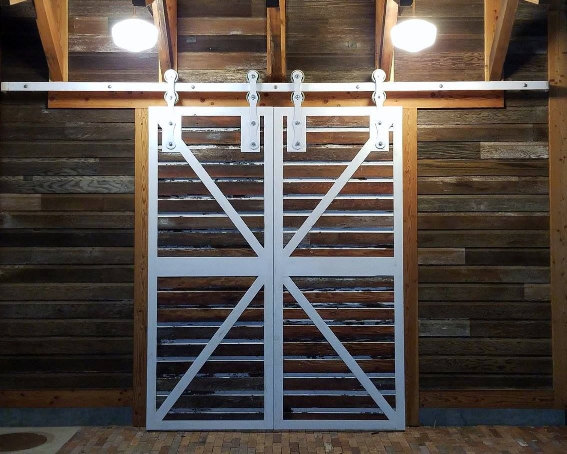 Barn door with metal frame and horizontal wooden slats, mounted on a track against a wooden wall, lit by two overhead lights.