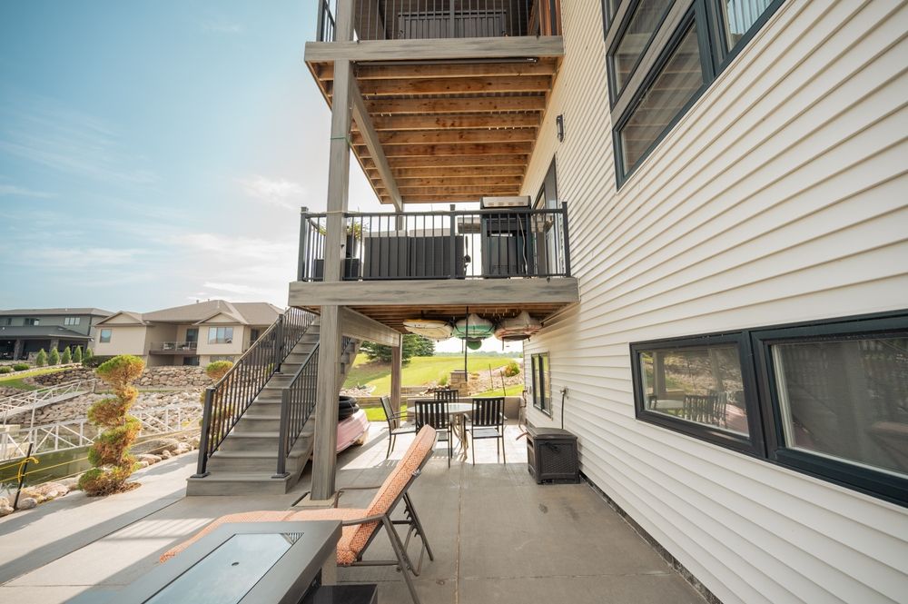 Two-story deck attached to a house with a lake view. Features stairs, outdoor furniture, and a grill.