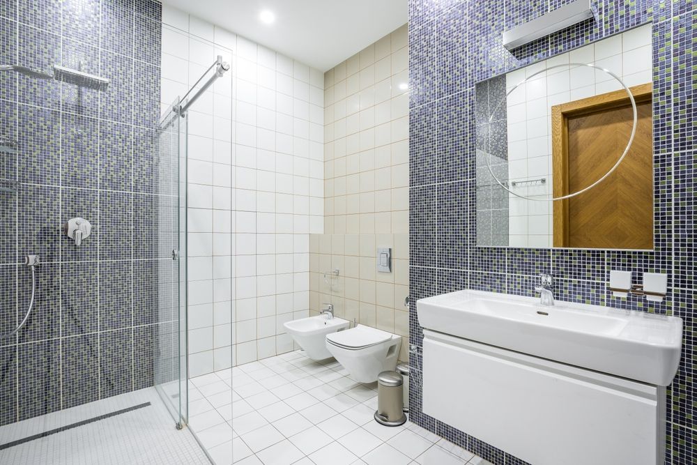 Modern bathroom with shower, toilet, and sink. Blue mosaic and white tile walls.