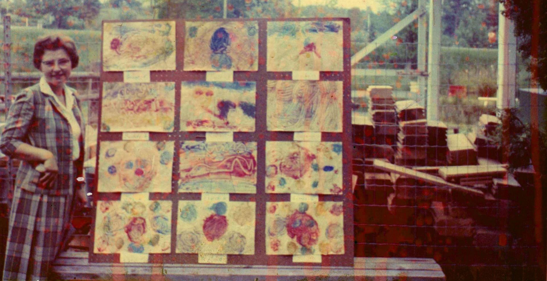 Montessori guide is standing in front of a display of children 's artwork.