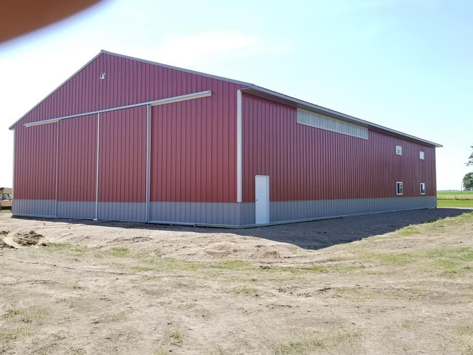 A large red barn is sitting in the middle of a dirt field.