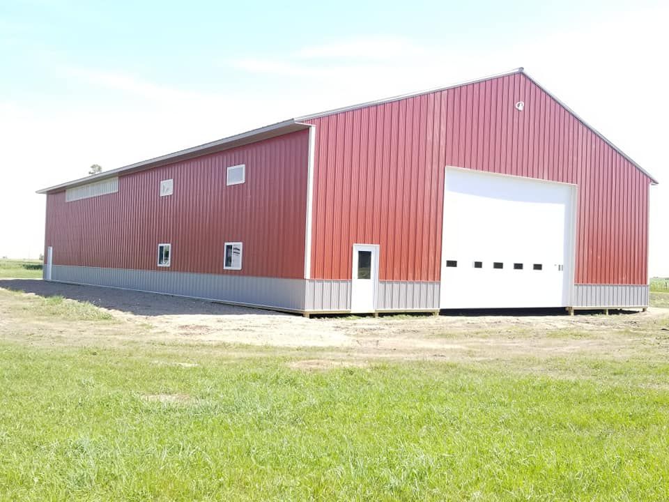 A large red barn with a white garage door is sitting in the middle of a grassy field.