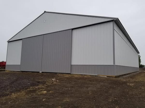A large white building with a sliding door is sitting in the middle of a dirt field.