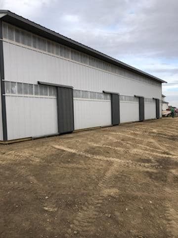 A large white building with sliding doors is sitting on top of a dirt field.
