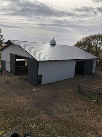 A large white barn with a gray roof is sitting on top of a dirt field.
