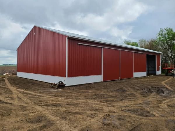 A large red barn is sitting in the middle of a dirt field.