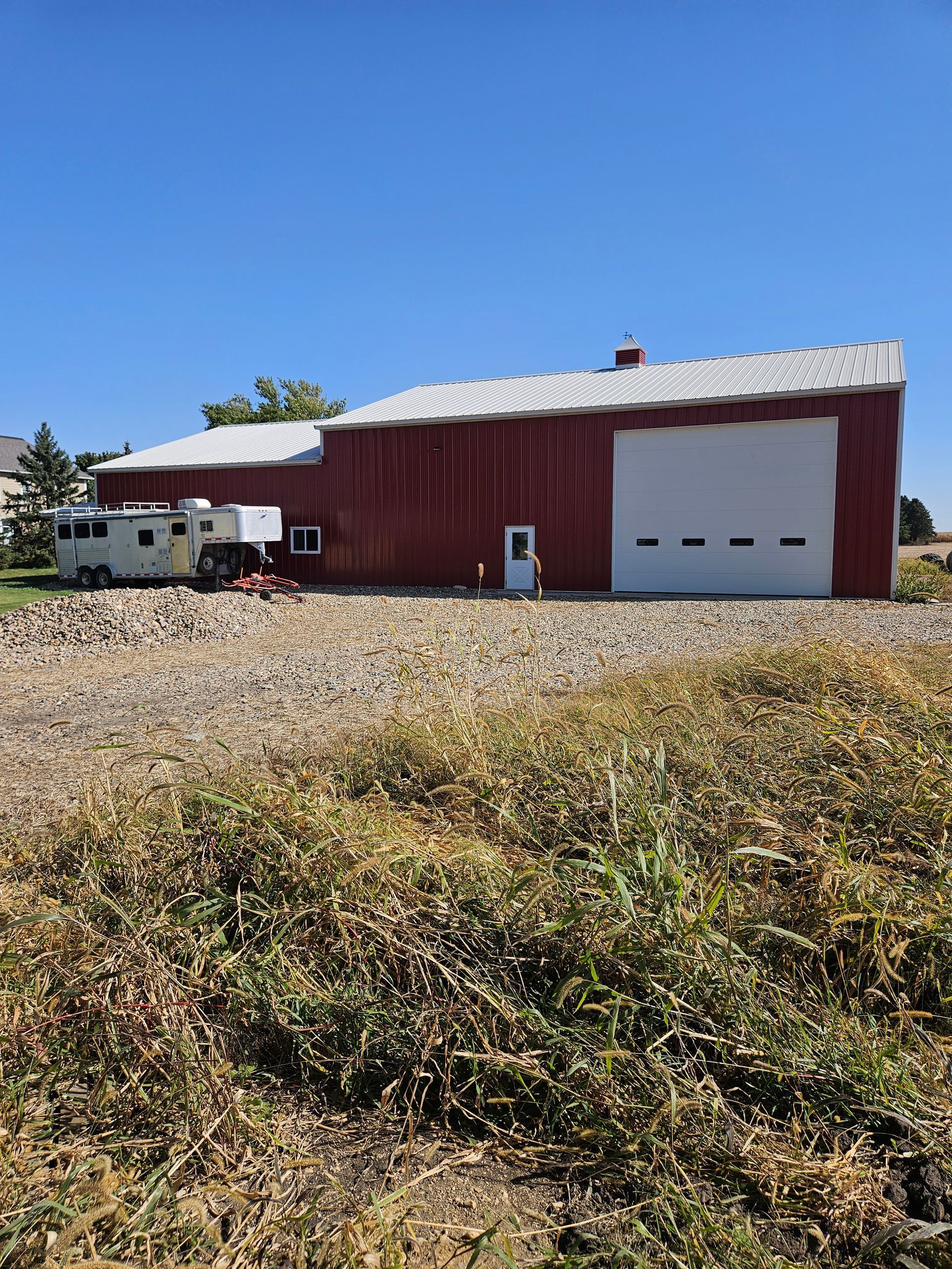 A red barn with a white garage door is sitting in the middle of a field.
