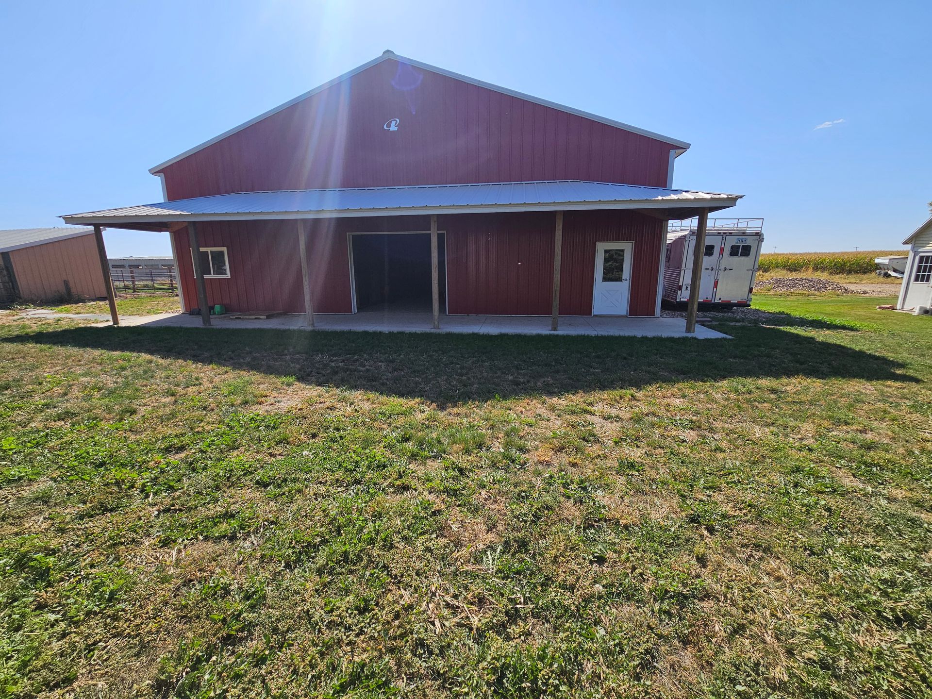 A red barn with a porch is sitting in the middle of a grassy field.