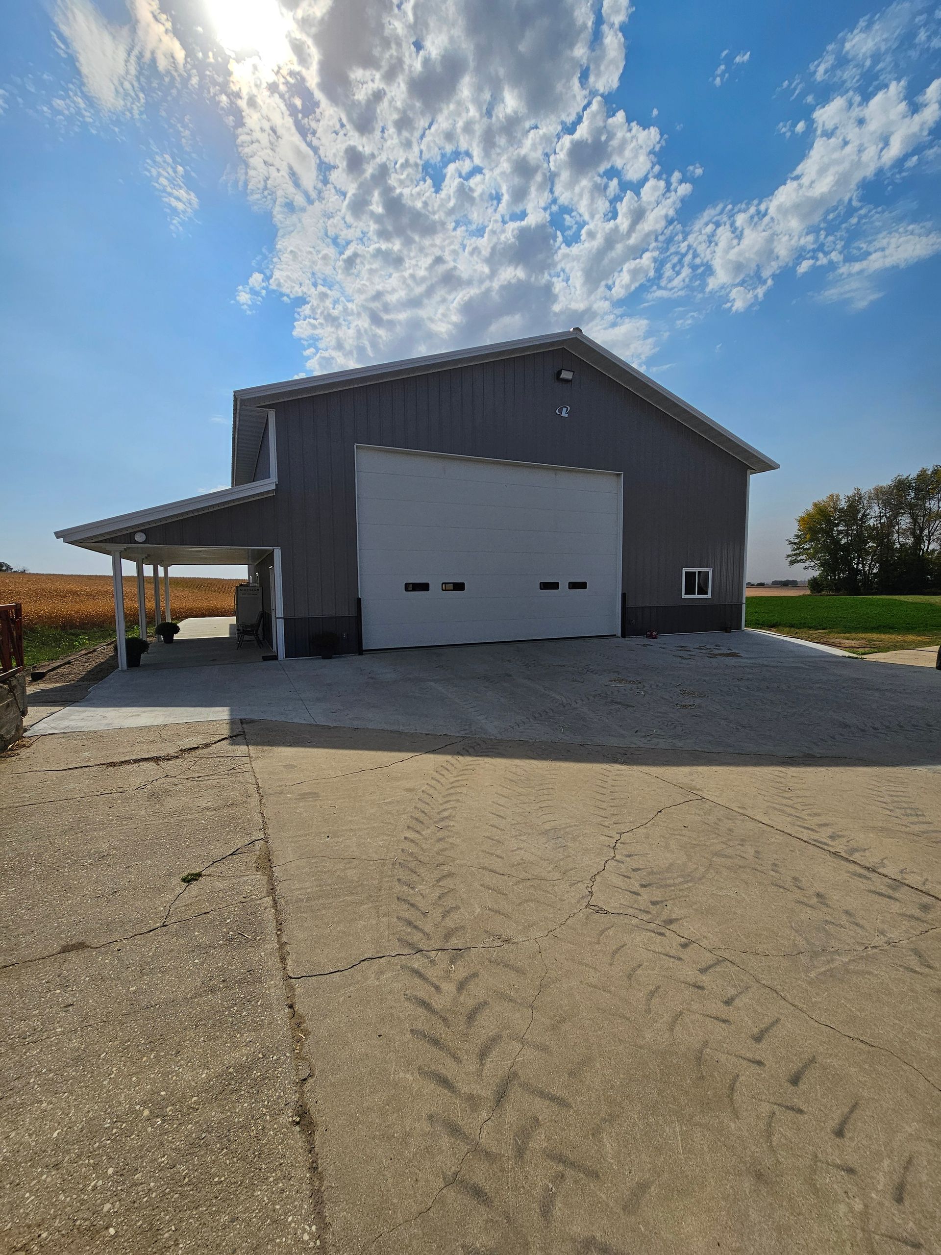 A large barn with a white garage door is sitting in the middle of a field.