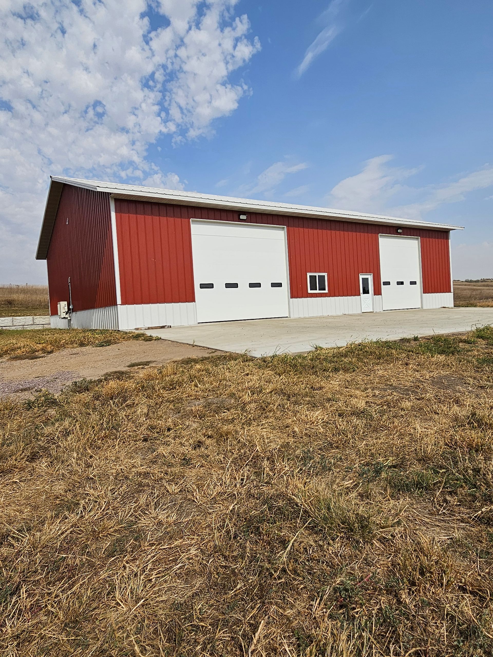 A red barn with white doors is in the middle of a field.