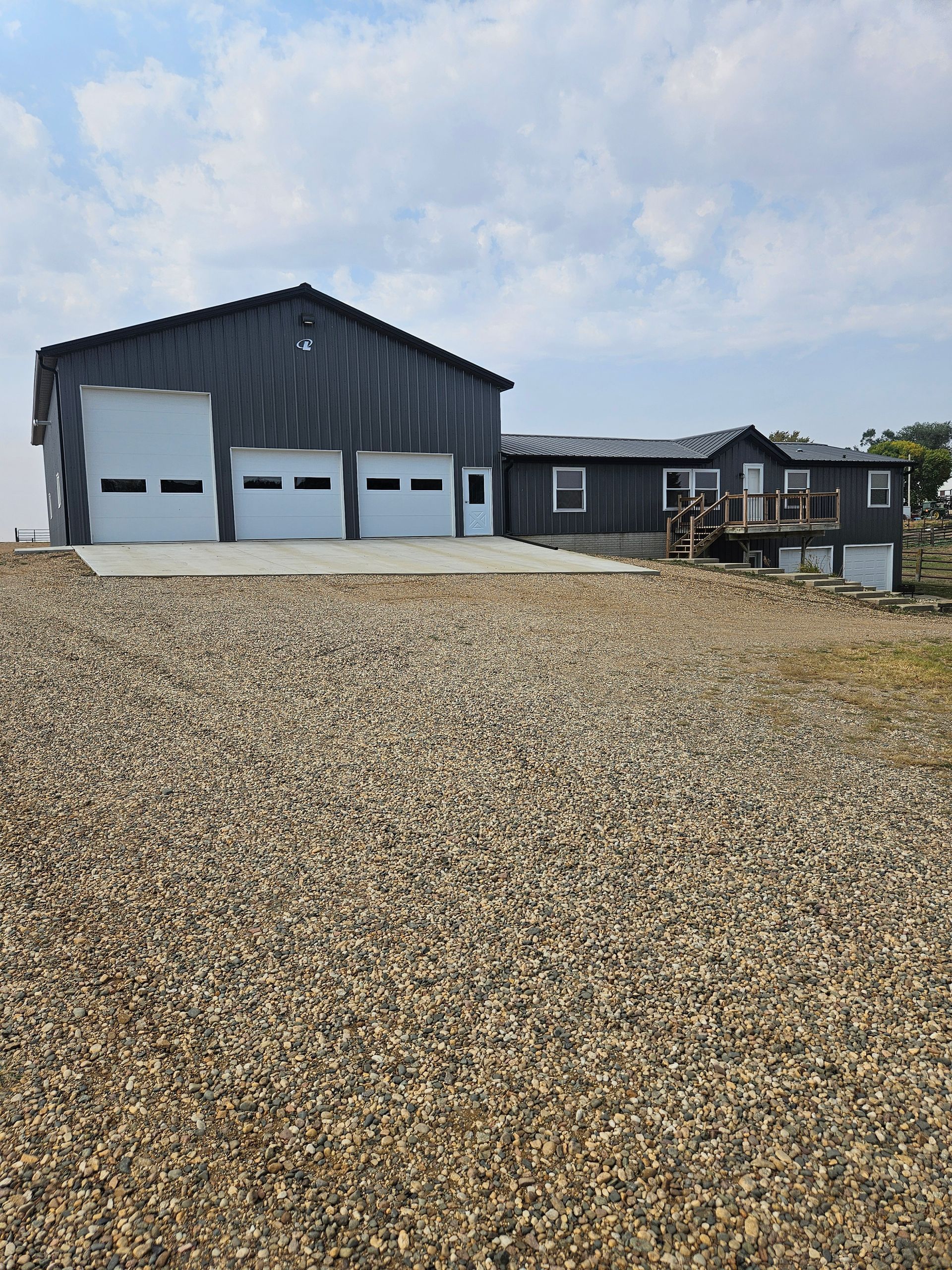 A large building with three garage doors is sitting on top of a gravel lot.
