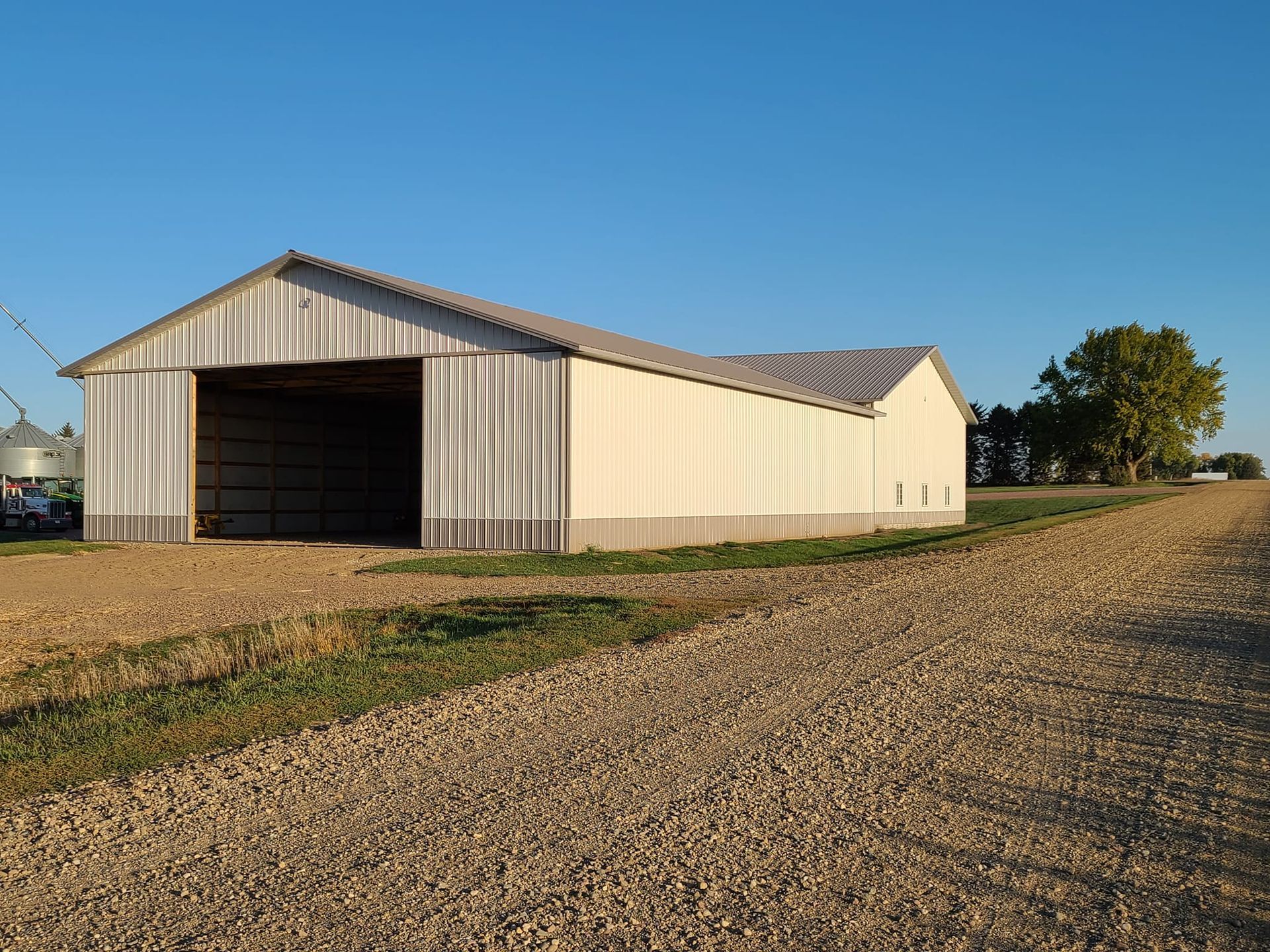 A large white barn is sitting on top of a gravel road.