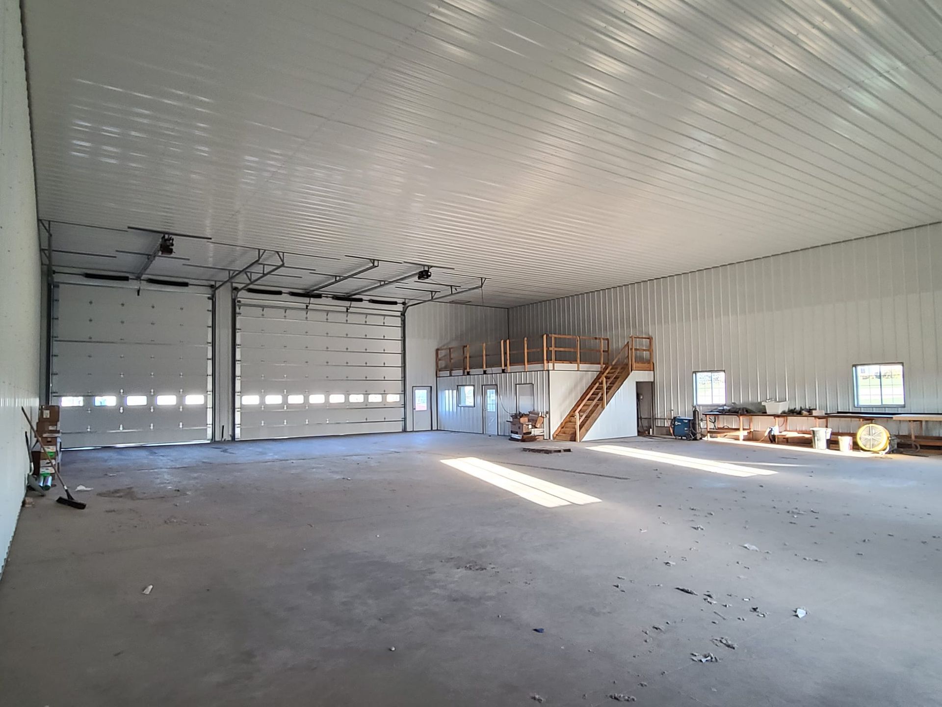 A large empty warehouse with a garage door and stairs.