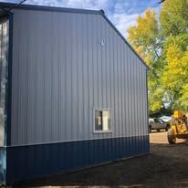 A blue and gray building with a yellow tractor parked in front of it.
