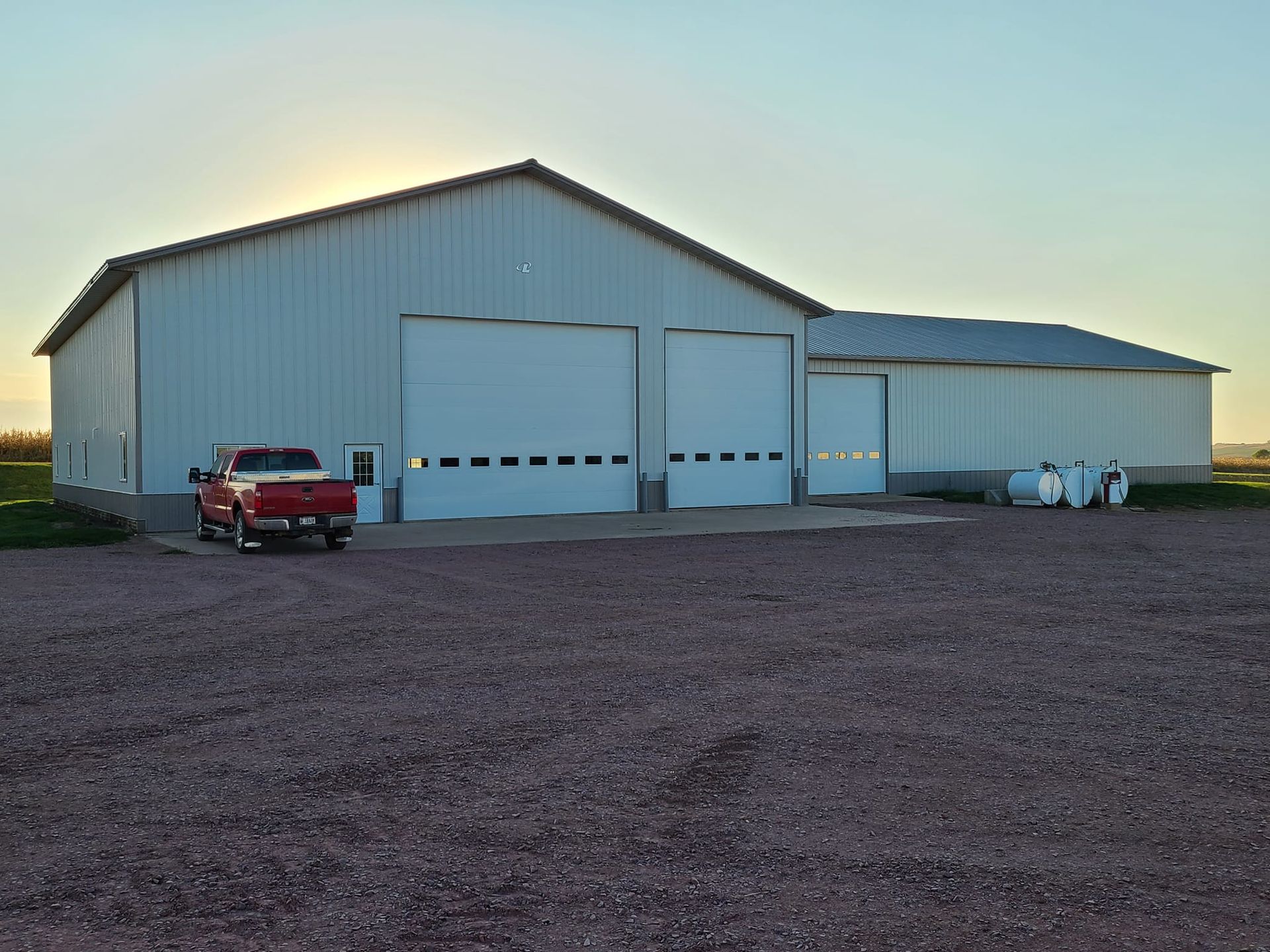A red truck is parked in front of a white barn