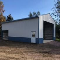A white and blue garage with a large door is sitting in the middle of a dirt field.